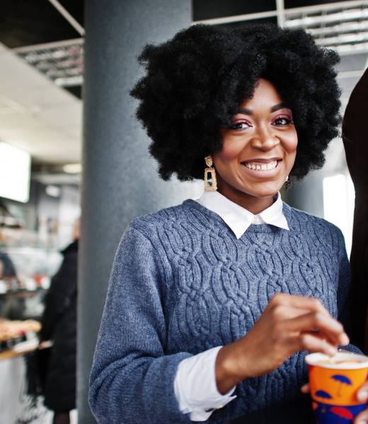 Curly hair african american woman wear on sweater posed at cafe indoor with cup of tea or coffee.